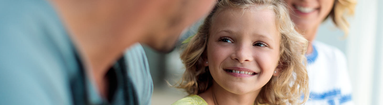 Young girl smiling with her parents in the background